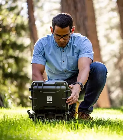 A photograph of a researcher in a forest setting up a SATURO infiltrometer