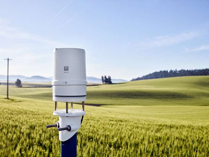 A photograph of an ATMOS 41 weather station mounted in the foreground with a field of wheat on rolling hills in the background