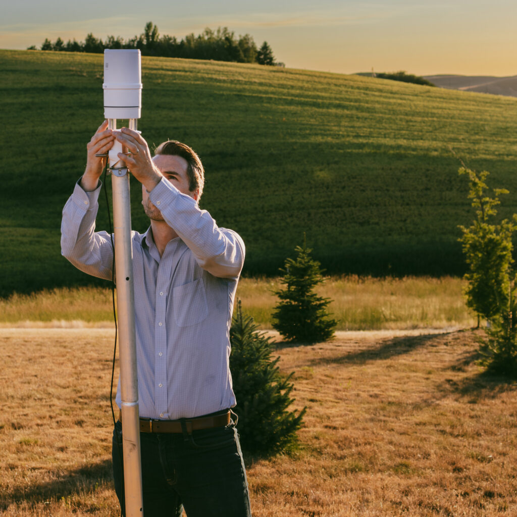 A photo of METER's atmospheric product manager, Jeff Ritter, installing an ATMOS 41 Gen 2 in a field at sunset